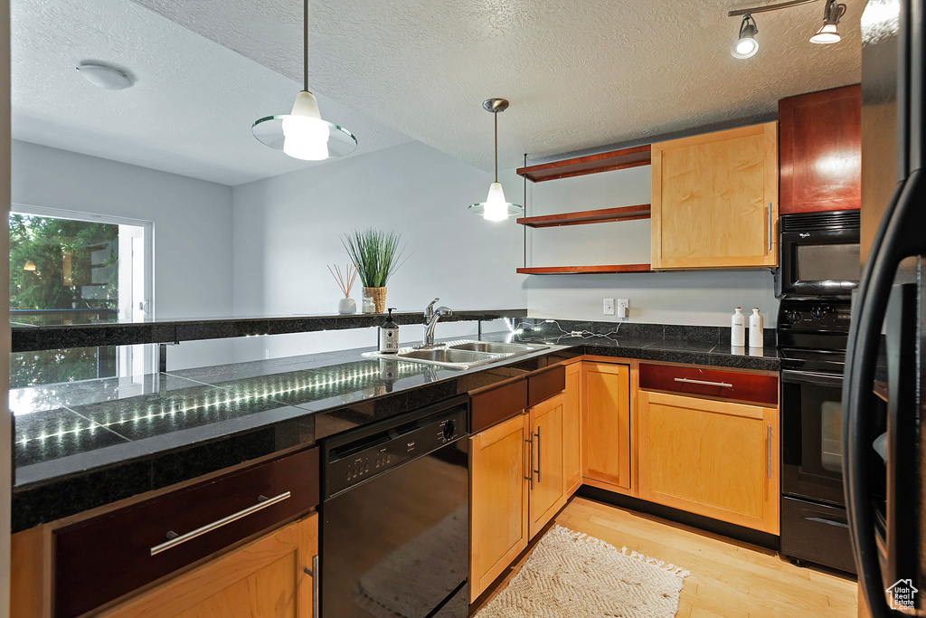 Kitchen featuring rail lighting, a textured ceiling, black appliances, pendant lighting, and sink