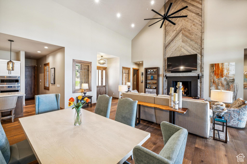 Dining room with ceiling fan, high vaulted ceiling, dark wood-type flooring, and a fireplace