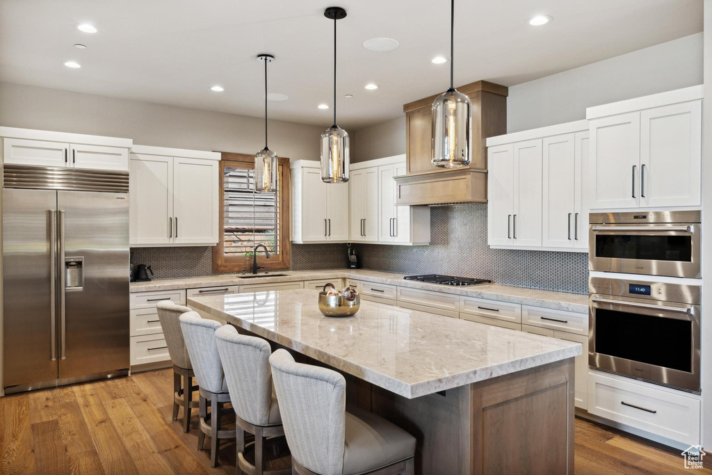 Kitchen featuring light wood-type flooring, stainless steel appliances, a center island, and decorative backsplash