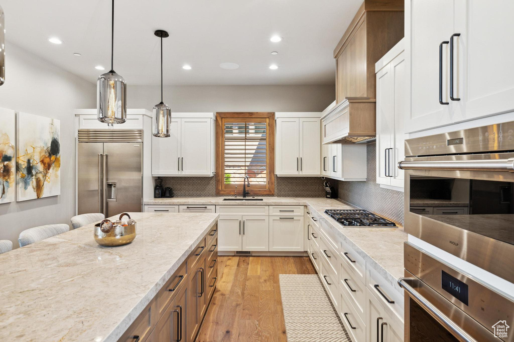 Kitchen with appliances with stainless steel finishes, white cabinets, light wood-type flooring, and tasteful backsplash