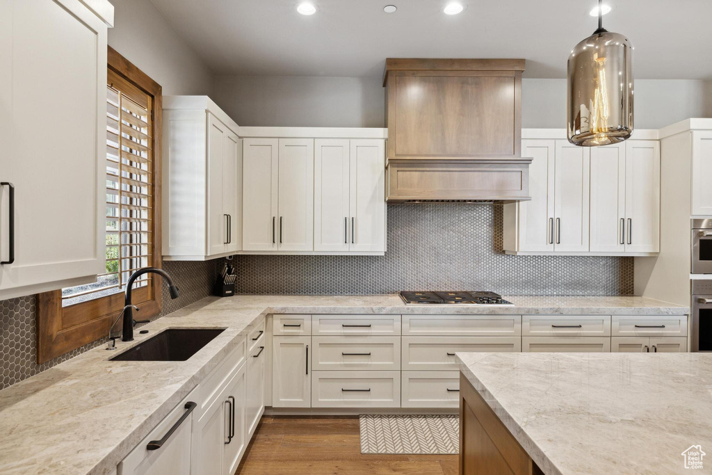 Kitchen featuring tasteful backsplash, light hardwood / wood-style floors, white cabinets, sink, and decorative light fixtures