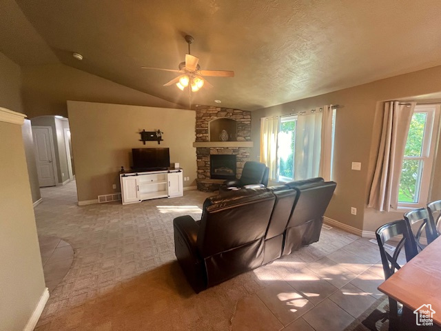 Living room featuring vaulted ceiling, a stone fireplace, carpet floors, ceiling fan, and a textured ceiling