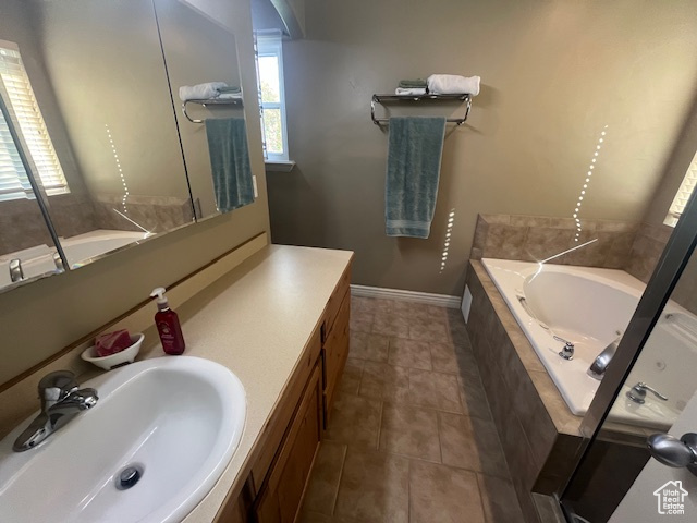 Bathroom with tile patterned flooring, tiled tub, and vanity