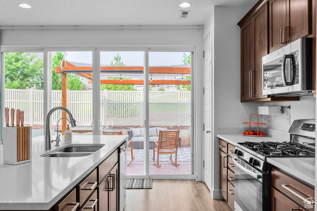 Kitchen with appliances with stainless steel finishes, sink, plenty of natural light, and light hardwood / wood-style floors