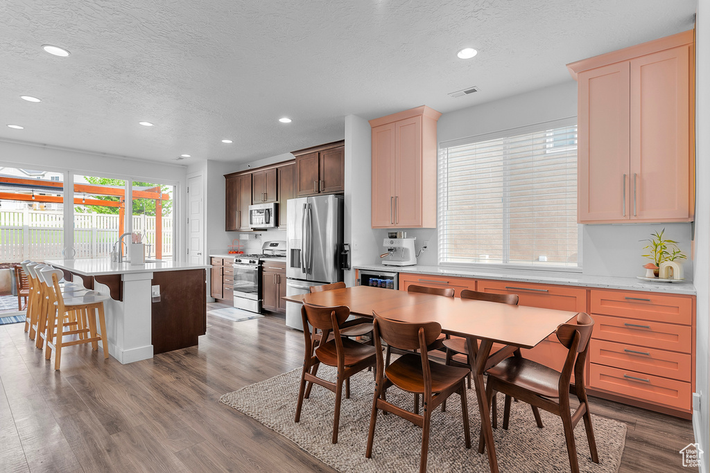 Kitchen with light brown cabinetry, dark brown cabinets, hardwood / wood-style flooring, a center island with sink, and stainless steel appliances