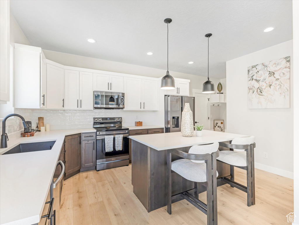 Kitchen with light wood-type flooring, stainless steel appliances, white cabinets, sink, and hanging light fixtures