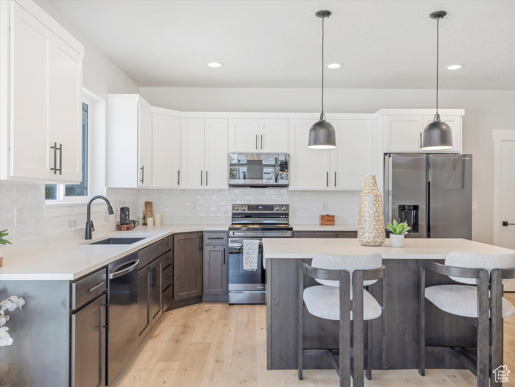 Kitchen with pendant lighting, sink, white cabinetry, stainless steel appliances, and a center island