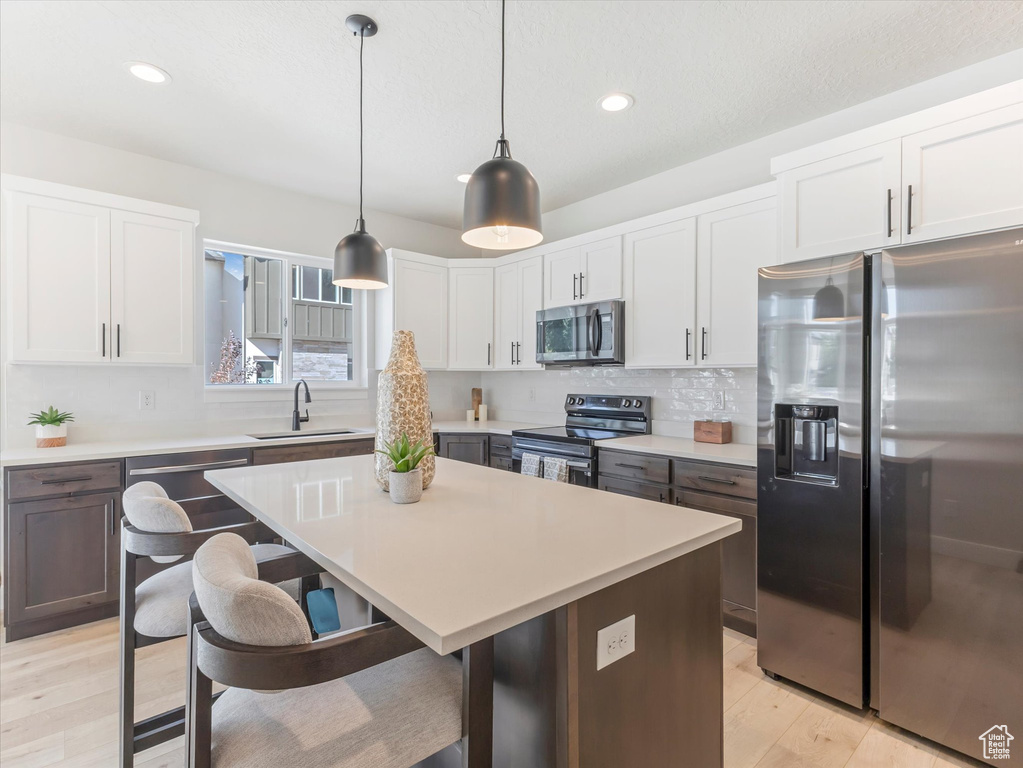 Kitchen with sink, decorative light fixtures, appliances with stainless steel finishes, a center island, and light hardwood / wood-style floors