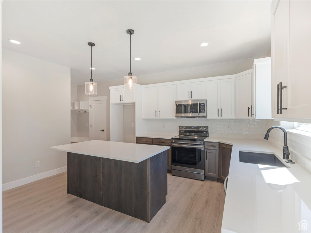 Kitchen with stainless steel appliances, a center island, sink, light hardwood / wood-style flooring, and decorative light fixtures