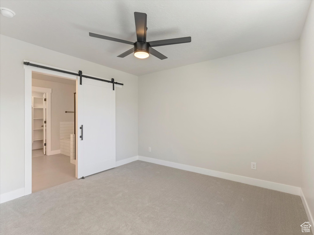 Unfurnished bedroom featuring a barn door, light colored carpet, ceiling fan, a spacious closet, and a closet