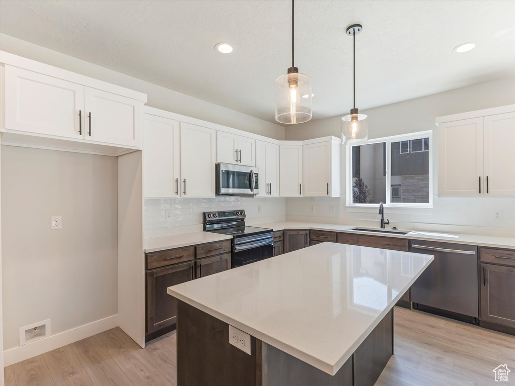 Kitchen featuring stainless steel appliances, light wood-type flooring, sink, white cabinetry, and decorative light fixtures