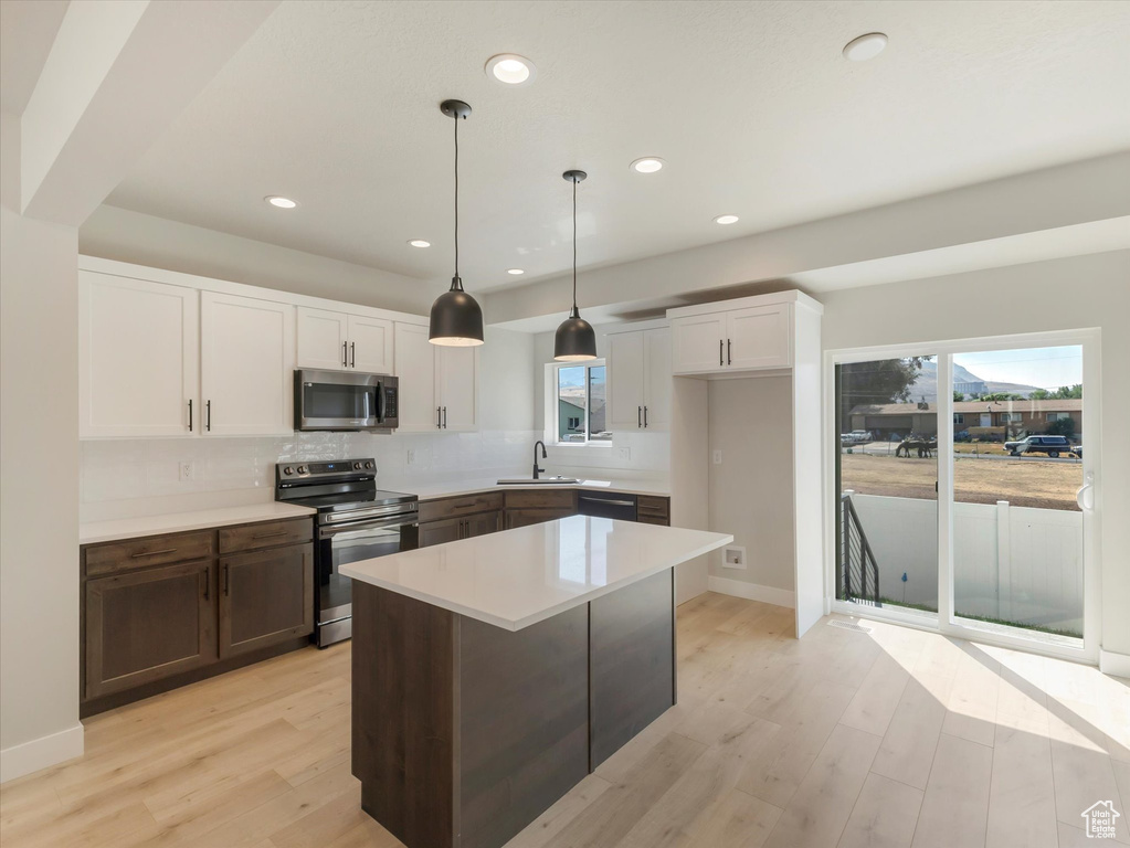 Kitchen with decorative backsplash, white cabinetry, pendant lighting, light hardwood / wood-style floors, and stainless steel appliances