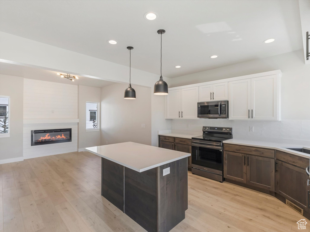 Kitchen featuring white cabinets, light wood-type flooring, a fireplace, and range with electric stovetop