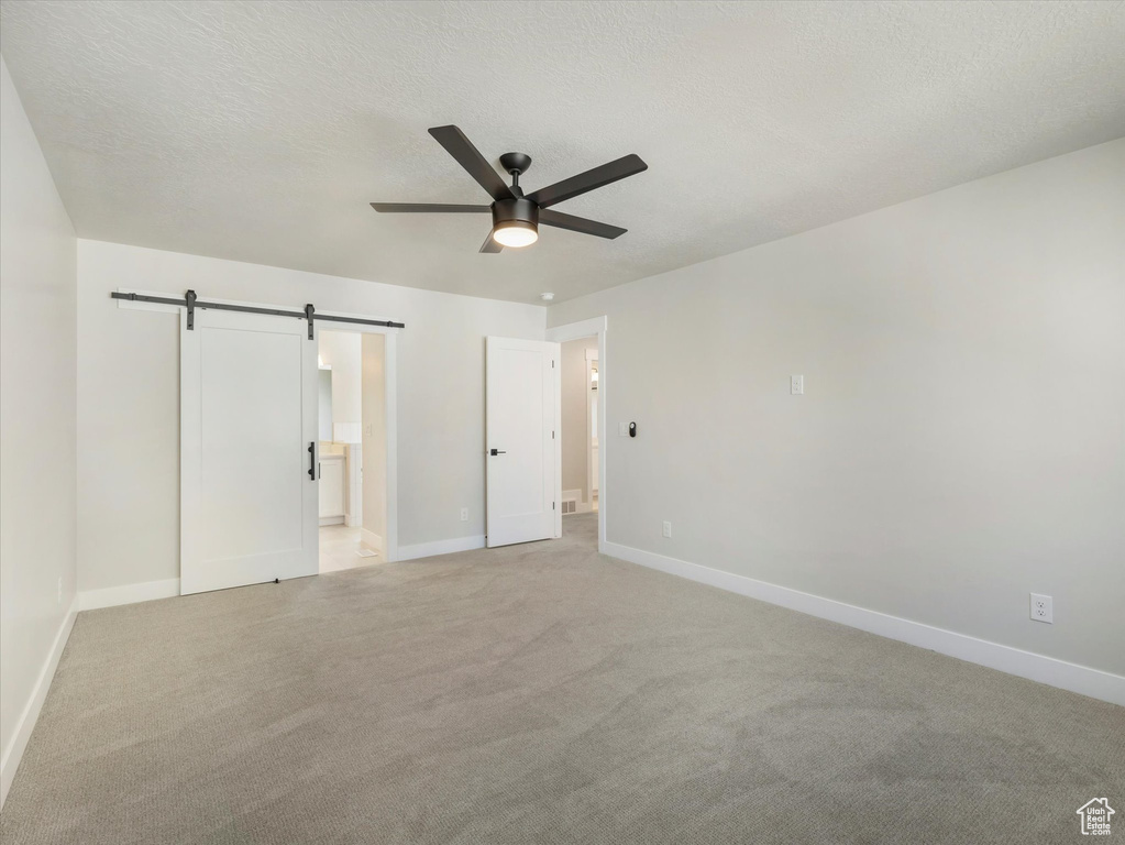 Unfurnished bedroom featuring light carpet, connected bathroom, a barn door, and ceiling fan