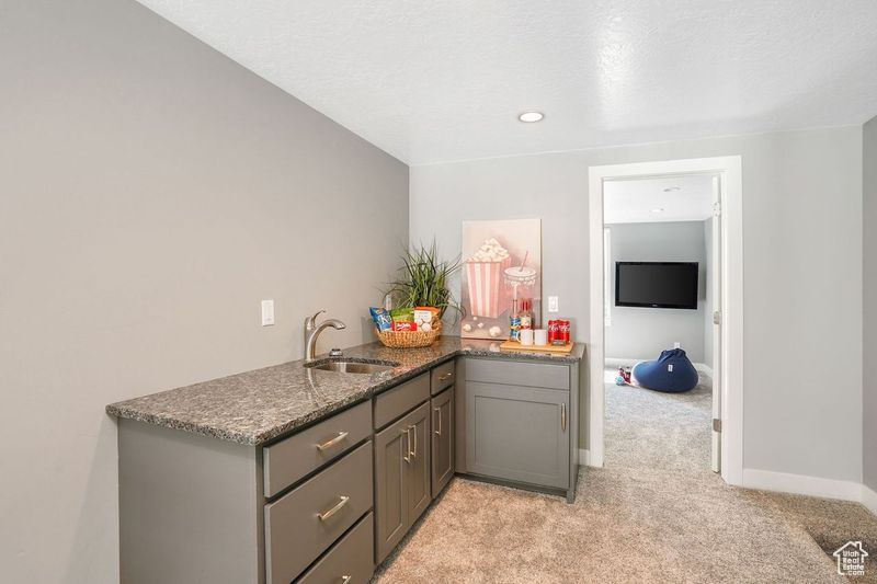 Kitchen with light colored carpet, gray cabinets, sink, dark stone counters, and kitchen peninsula