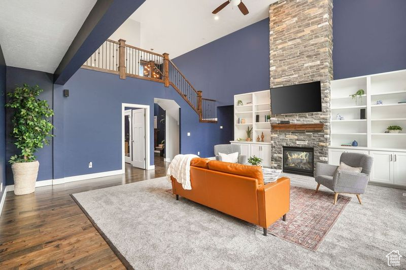 Living room with ceiling fan, a fireplace, hardwood / wood-style flooring, and a towering ceiling