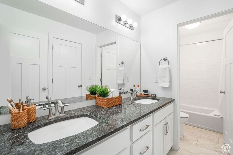 Full bathroom featuring tub / shower combination, toilet, dual bowl vanity, and tile patterned flooring