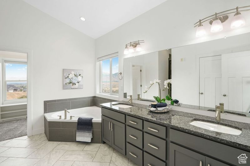 Bathroom with double sink vanity, tiled tub, tile patterned floors, and lofted ceiling