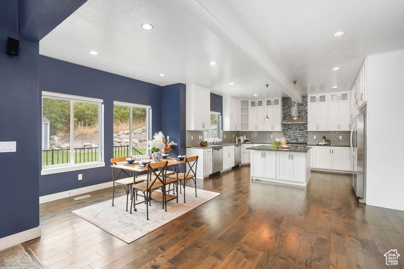 Kitchen featuring appliances with stainless steel finishes, white cabinets, wall chimney range hood, dark wood-type flooring, and a kitchen island