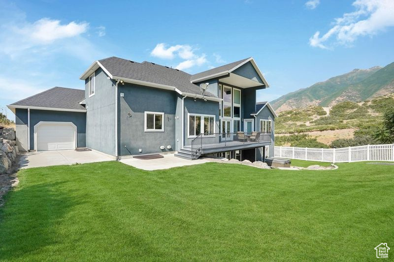 Rear view of property with a deck with mountain view, a yard, and a garage