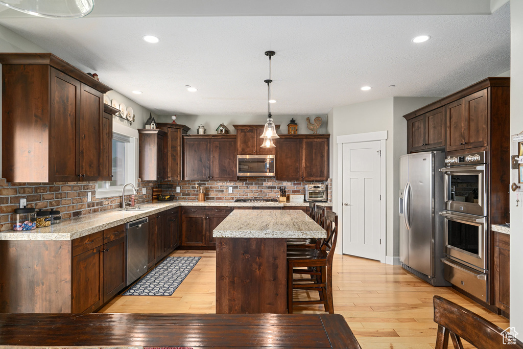 Kitchen featuring decorative backsplash, light hardwood / wood-style flooring, hanging light fixtures, stainless steel appliances, and a breakfast bar area