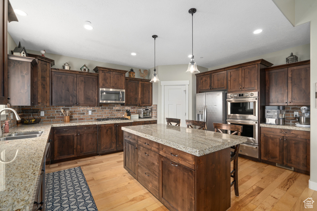 Kitchen featuring decorative backsplash, light hardwood / wood-style flooring, stainless steel appliances, and a breakfast bar