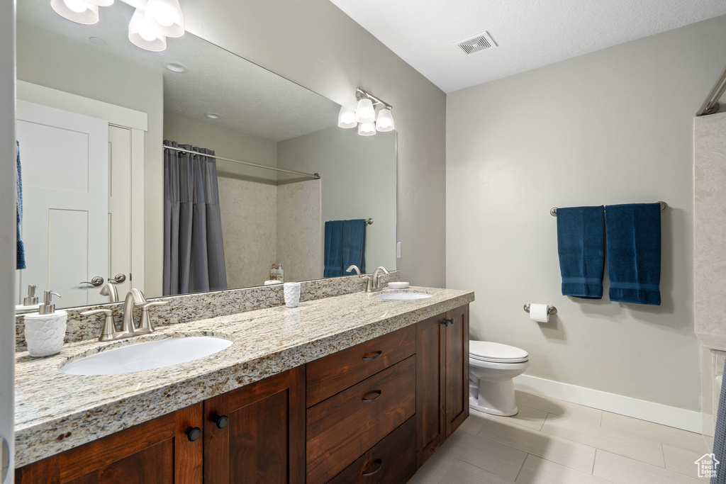 Bathroom with tile patterned floors, dual bowl vanity, and toilet