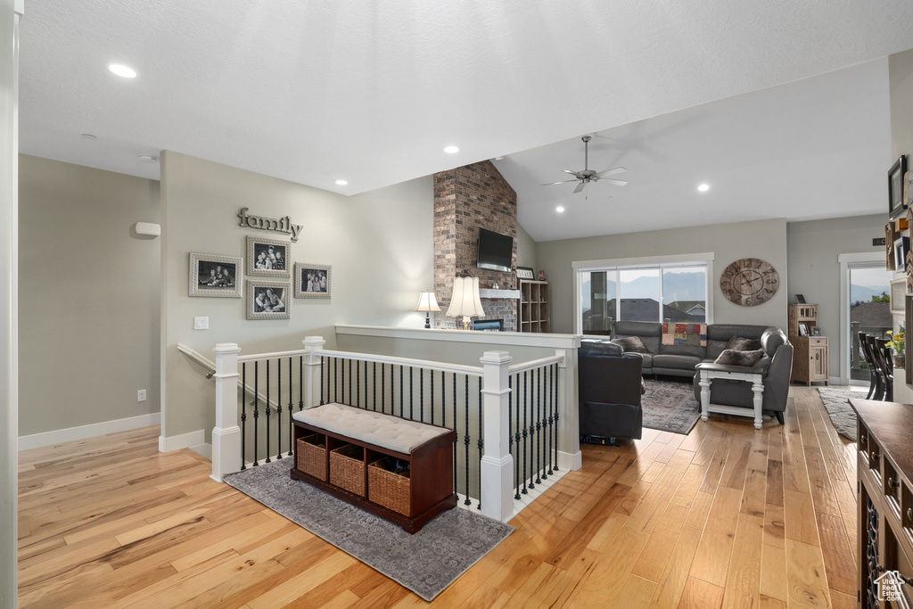 Living room featuring ceiling fan, light wood-type flooring, lofted ceiling, and brick wall