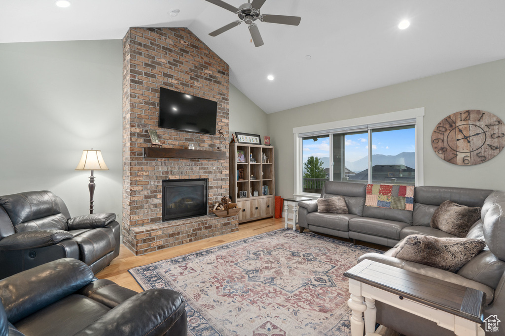 Living room featuring a brick fireplace, brick wall, light wood-type flooring, and ceiling fan