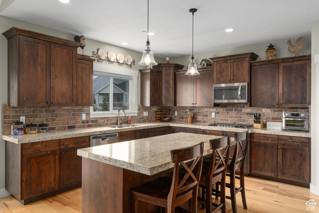 Kitchen with sink, stainless steel appliances, light hardwood / wood-style flooring, and decorative backsplash