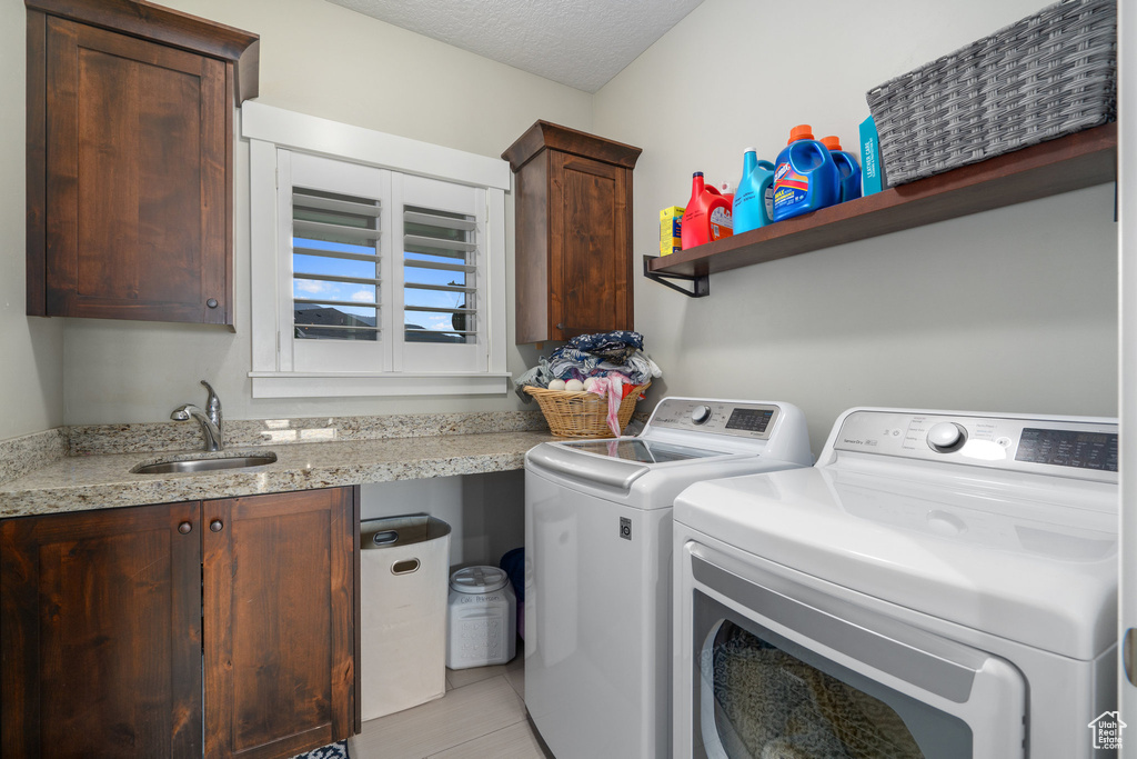 Laundry area featuring cabinets, a textured ceiling, independent washer and dryer, light tile patterned floors, and sink