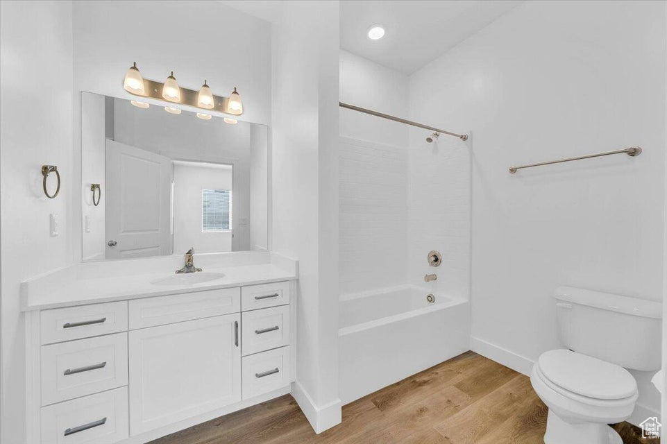 Full bathroom with hardwood / wood-style floors, shower / bathtub combination, vanity, and toilet