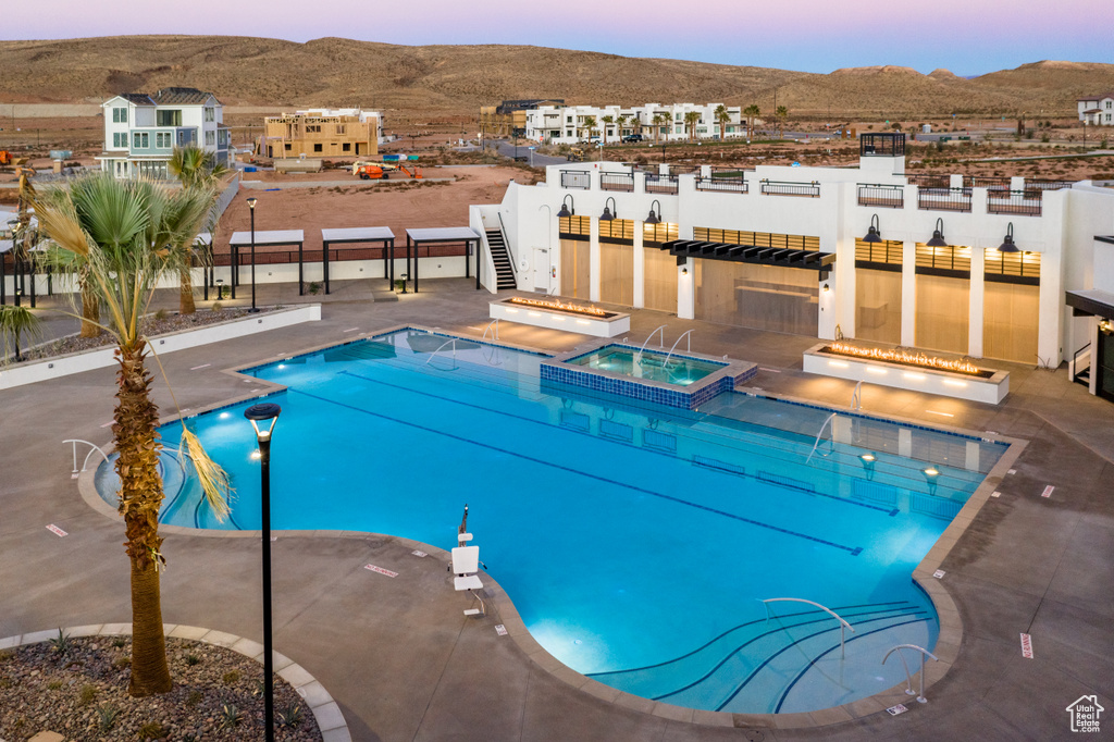 Pool at dusk with an outdoor bar, a mountain view, a hot tub, and a patio area