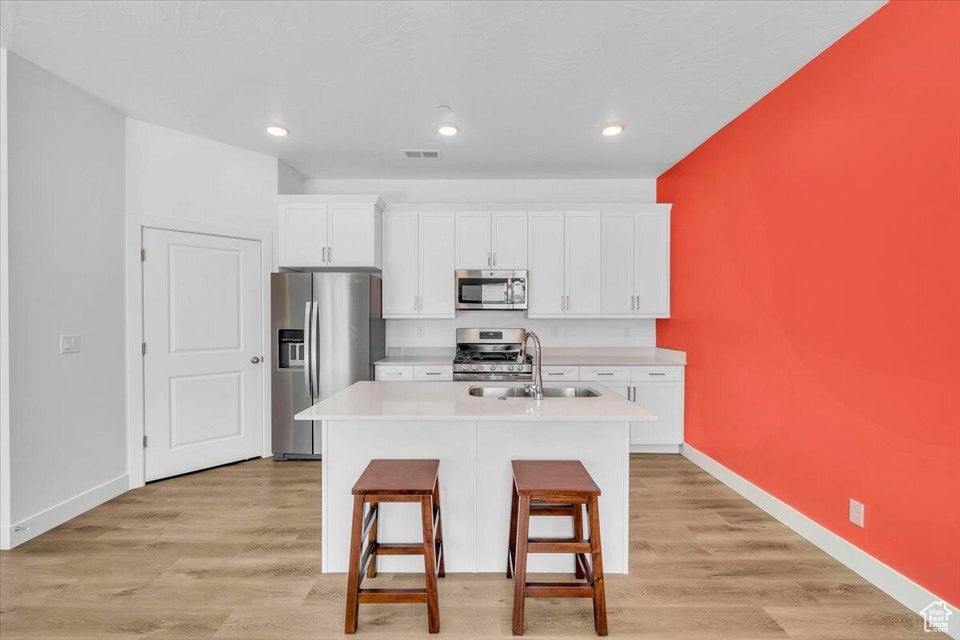 Kitchen featuring a center island with sink, sink, stainless steel appliances, and light hardwood / wood-style floors