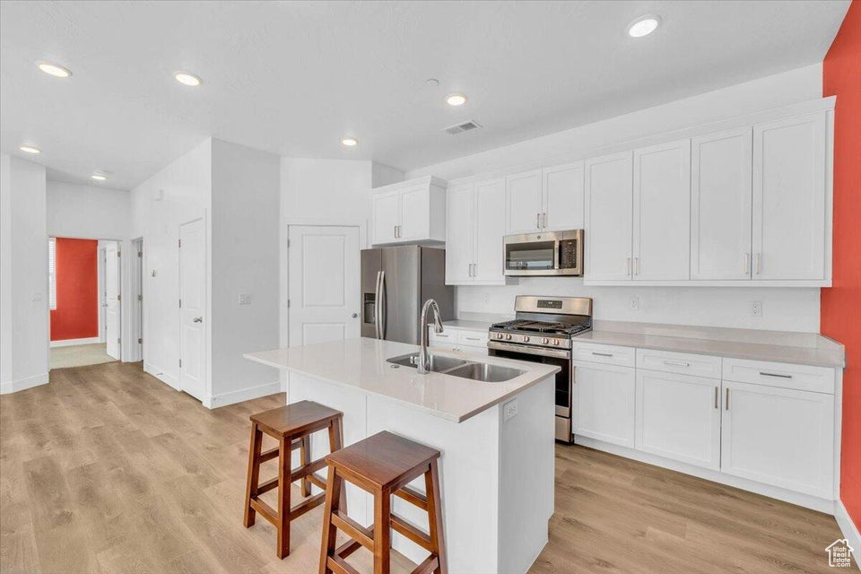 Kitchen with white cabinets, a kitchen island with sink, light wood-type flooring, stainless steel appliances, and sink