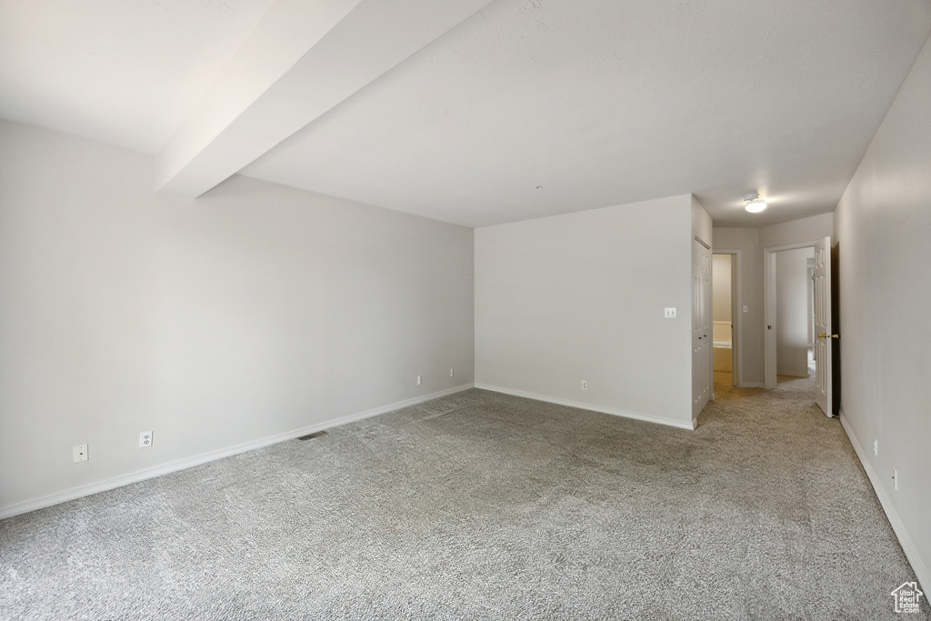 Unfurnished room with light carpet and beamed ceiling