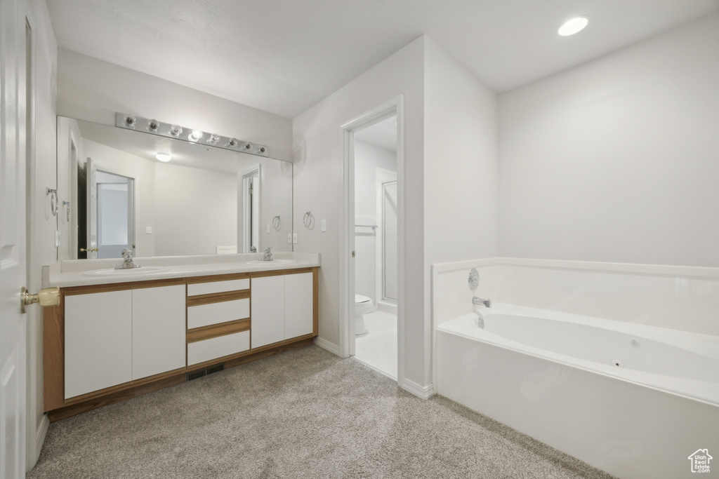 Bathroom featuring dual bowl vanity, a tub, and toilet