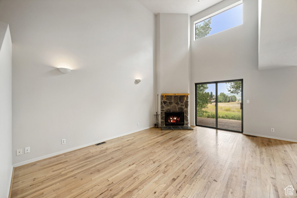 Unfurnished living room with light hardwood / wood-style flooring, a stone fireplace, and a towering ceiling