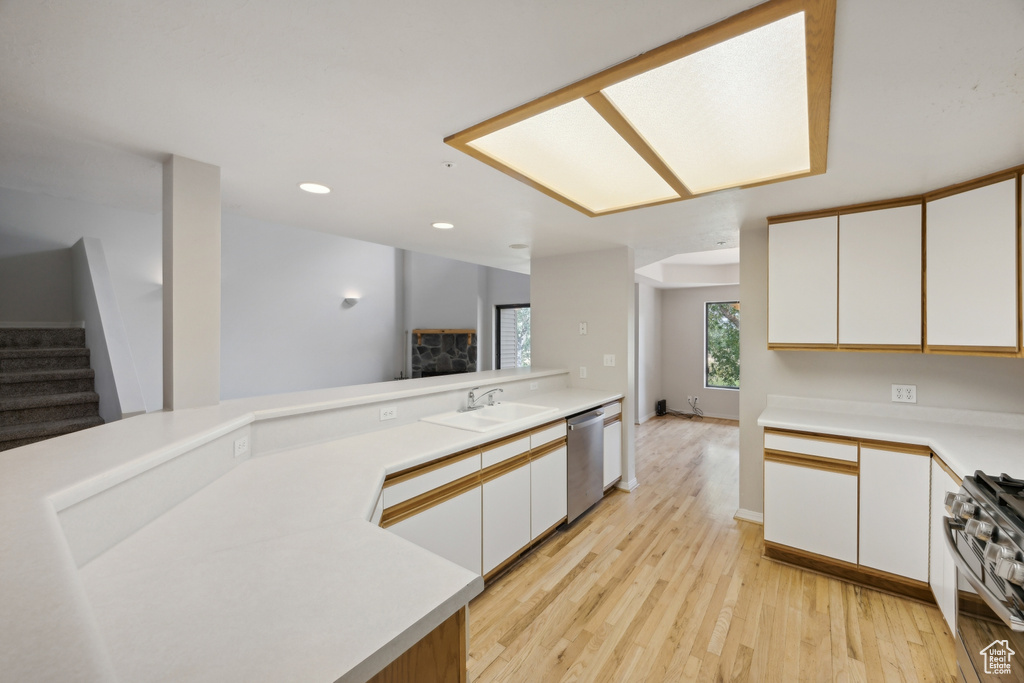 Kitchen with stainless steel appliances, white cabinets, sink, light hardwood / wood-style flooring, and kitchen peninsula