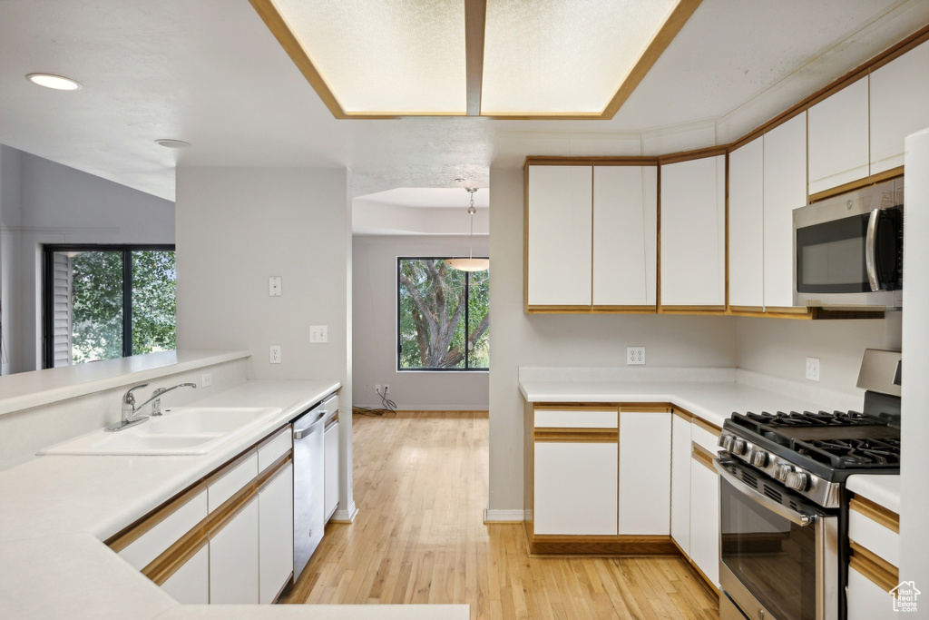 Kitchen with appliances with stainless steel finishes, light wood-type flooring, a wealth of natural light, and white cabinets