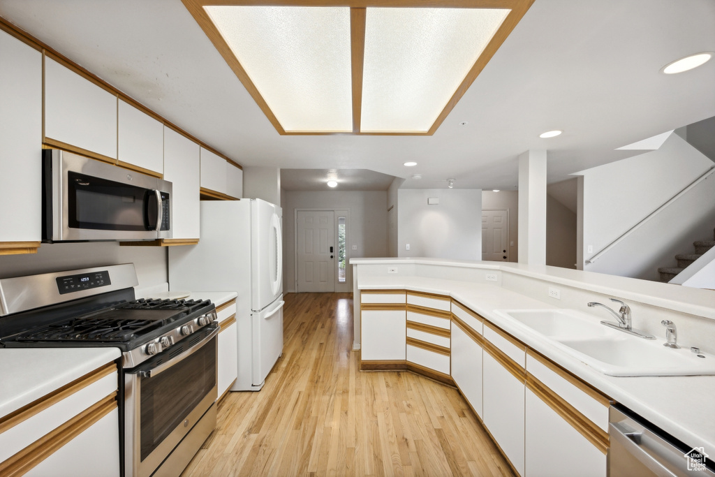 Kitchen with stainless steel appliances, white cabinetry, light hardwood / wood-style flooring, sink, and kitchen peninsula