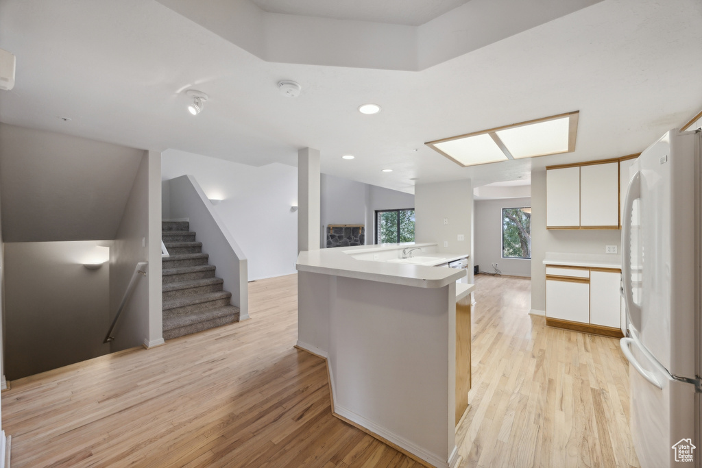 Kitchen with a center island with sink, light hardwood / wood-style floors, sink, white cabinets, and white fridge