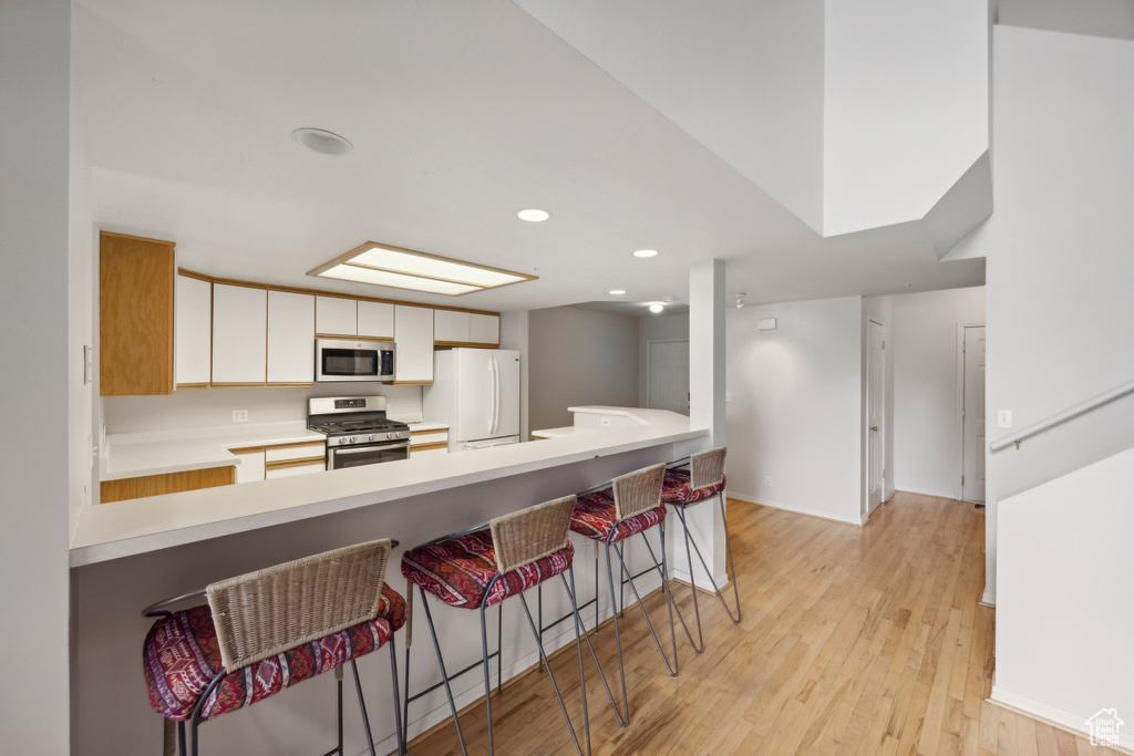 Kitchen featuring a breakfast bar area, stainless steel appliances, light hardwood / wood-style floors, white cabinetry, and kitchen peninsula