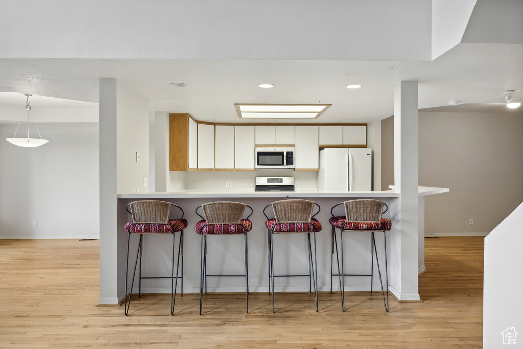 Kitchen featuring white cabinetry, white fridge, light hardwood / wood-style flooring, a kitchen bar, and kitchen peninsula