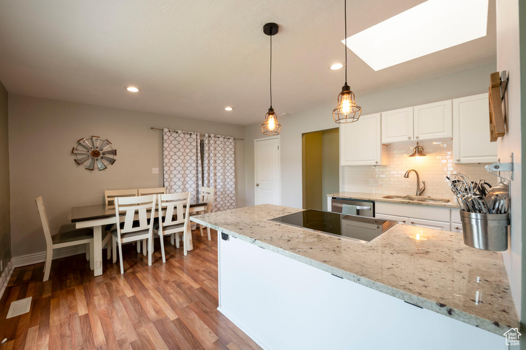 Kitchen featuring light hardwood / wood-style floors, white cabinetry, light stone counters, a skylight, and decorative light fixtures