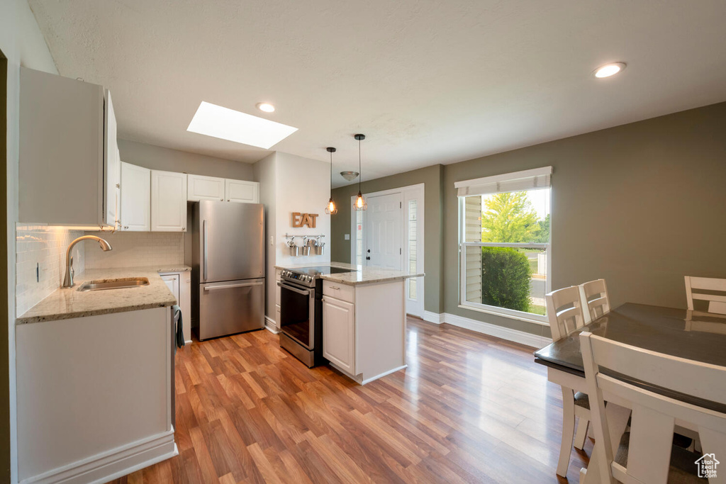 Kitchen with appliances with stainless steel finishes, hanging light fixtures, white cabinets, a skylight, and sink