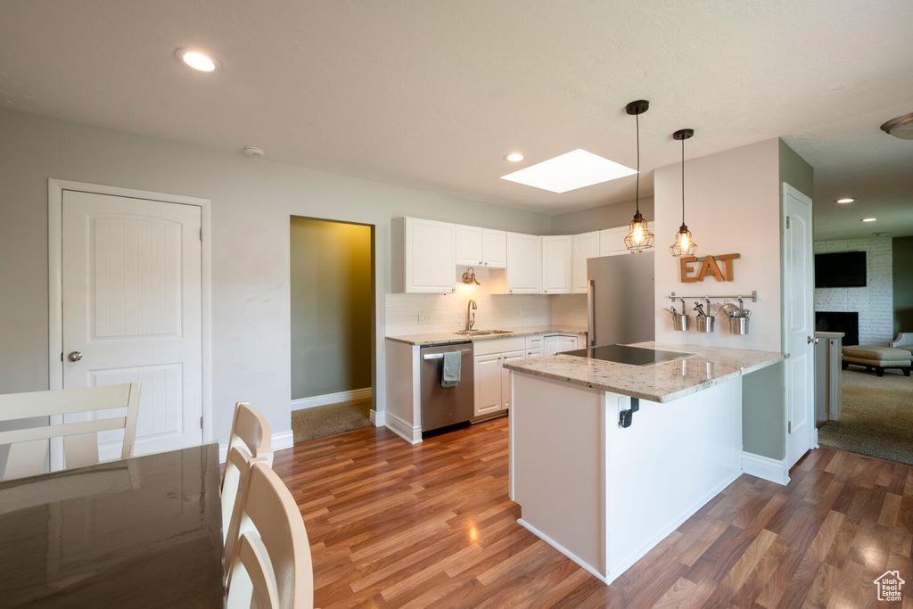 Kitchen with hardwood / wood-style flooring, appliances with stainless steel finishes, a breakfast bar, and white cabinetry