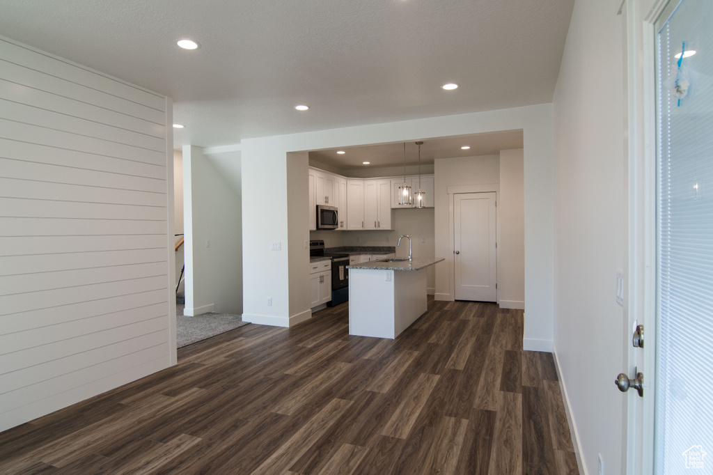 Kitchen featuring a center island with sink, dark hardwood / wood-style flooring, electric range oven, hanging light fixtures, and white cabinetry