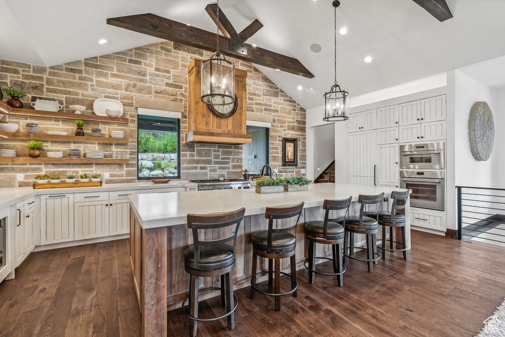 Kitchen with dark hardwood / wood-style flooring, double oven, a center island, and lofted ceiling with beams