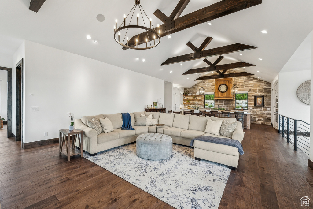 Living room featuring wood-type flooring, ceiling fan with notable chandelier, vaulted ceiling with beams, and brick wall